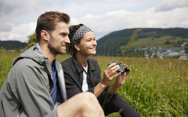 Mann und Frau mit Fernglas sitzen auf einer Blumenwiese im Sauerland