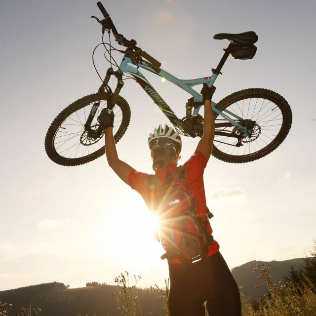 Radfahrerin hält Mountainbike vor untergehender Sonne in die Höhe